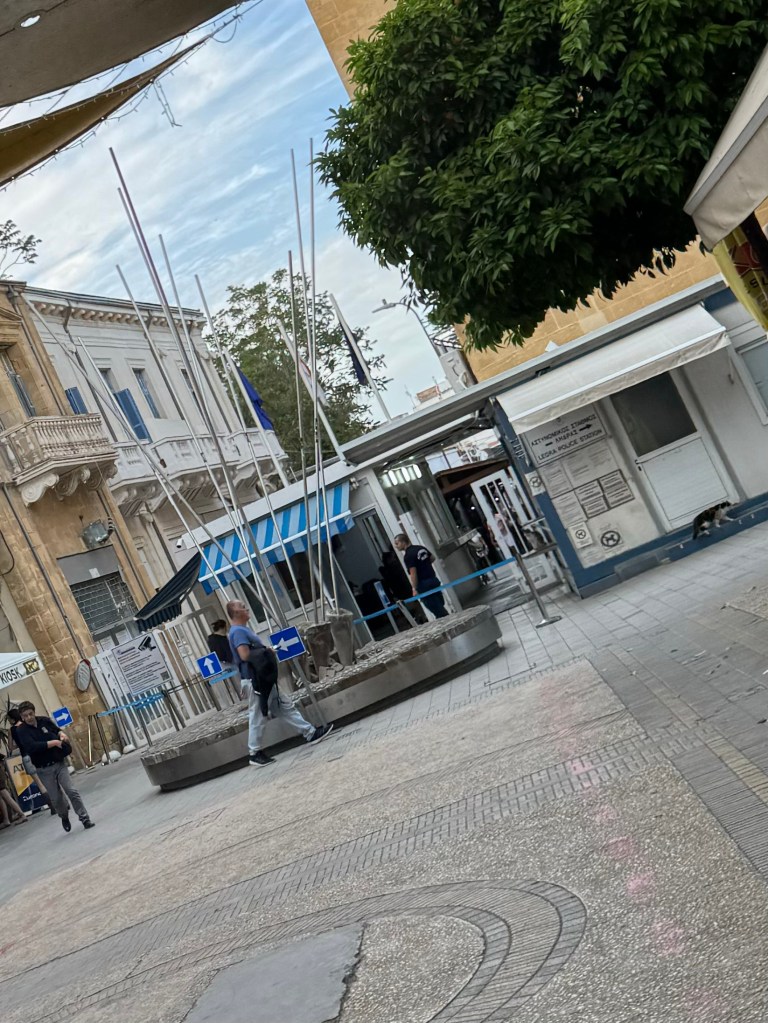 Punto di controllo al confine tra le parti greca e turca di Nicosia, Cipro, con passanti e bandiere visibili.
